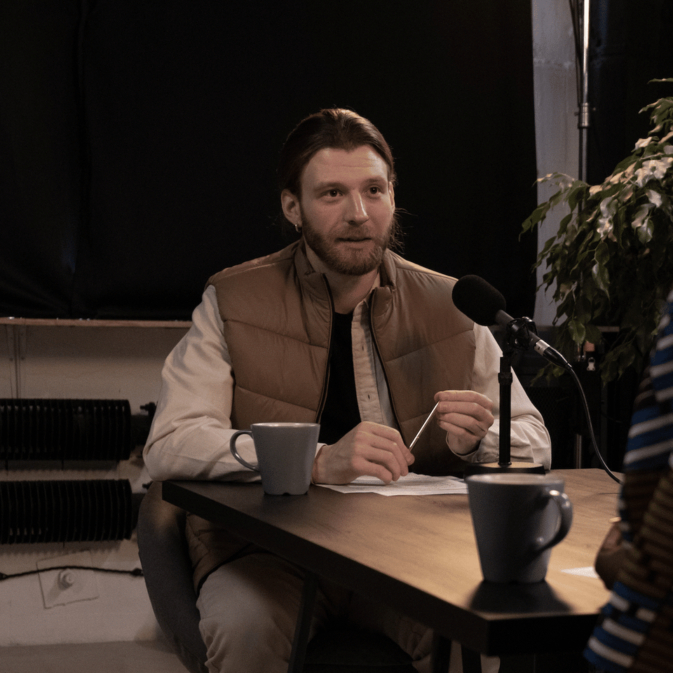 Ein Mann berichtet in einer Interview-Situation an einem Tisch mit Mikrofon über seine Erfahrungen