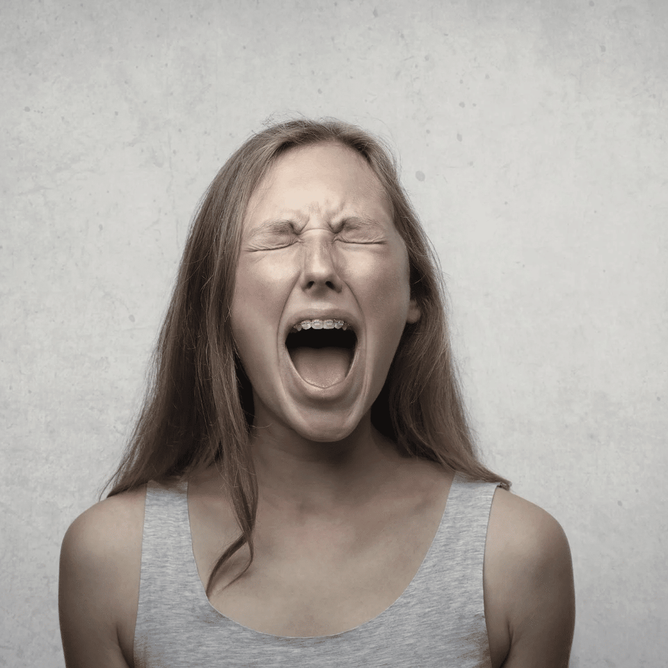 Eine schreiende junge Frau mit zusammengekniffenen Augen zur Veranschaulichung des Erkennens von Emotionen