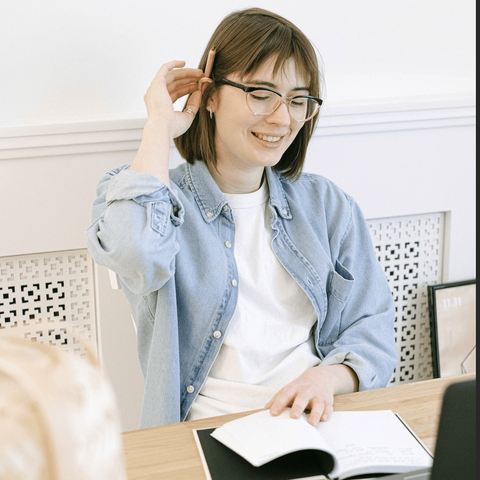 Eine lächelnde junge Frau mit Brille lernt mit einem Notizbuch für die TOEFL-Testvorbereitung
