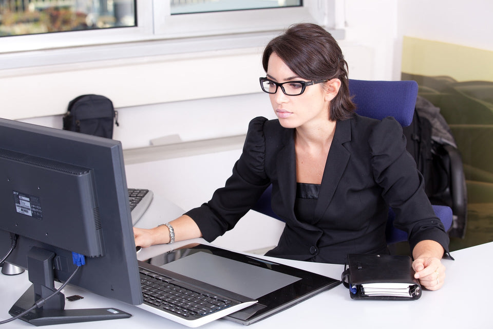 Eine Frau im schwarzen Blazer arbeitet konzentriert am Computer im Büro