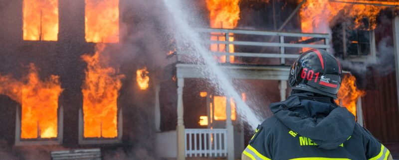 Feuerwehrmann im Einsatz löscht ein brennendes Haus mit einem Wasserstrahl