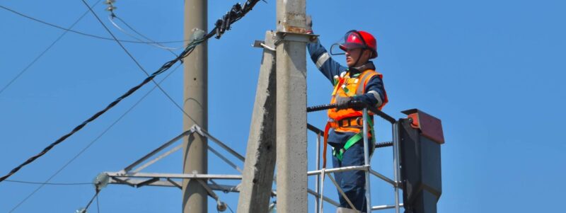 Elektroniker in Arbeitsbühne bei Wartungsarbeiten an einem Strommast