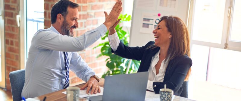 Zwei lächelnde Personen im Business-Outfit klatschen sich im Büro erfolgreich ab