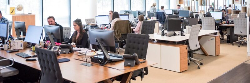 Mitarbeiter in einem modernen Großraumbüro an ihren Computerarbeitsplätzen als Symbol für die Arbeit in der Verwaltung