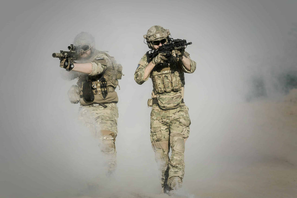 Zwei Soldaten in Tarnkleidung und voller Ausrüstung rücken mit Gewehren im Anschlag durch dichten Rauch vor