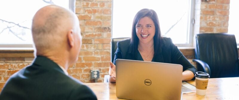 Eine lächelnde Frau im Bewerbungsgespräch mit einem Mann am Laptop