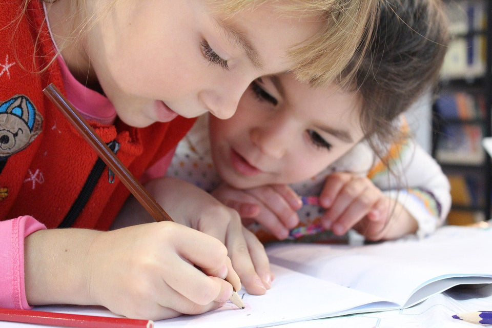 Zwei Kinder malen konzentriert mit Buntstiften in ein Heft als Symbol für die Vorbereitung auf die Schule