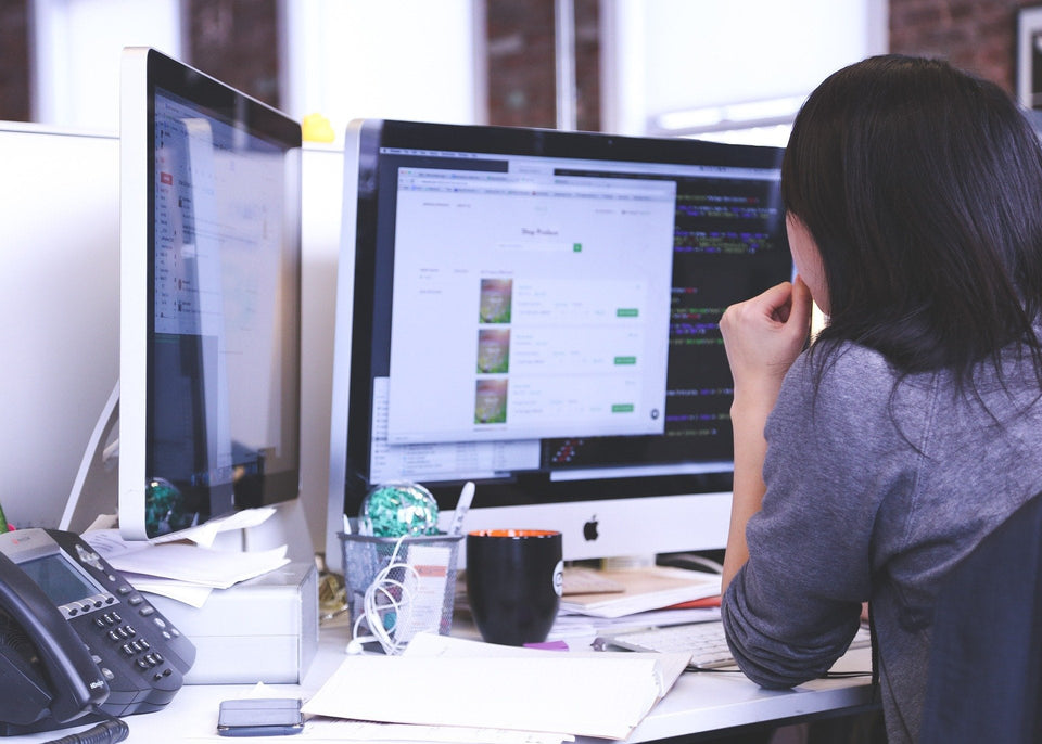 Eine Frau arbeitet konzentriert an zwei großen Computerbildschirmen am Schreibtisch