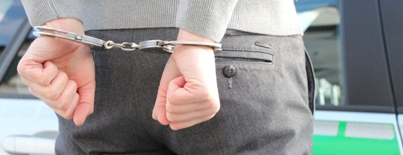 Festgenommene Person in Handschellen vor einem Polizeifahrzeug zur Veranschaulichung polizeilicher Arbeit