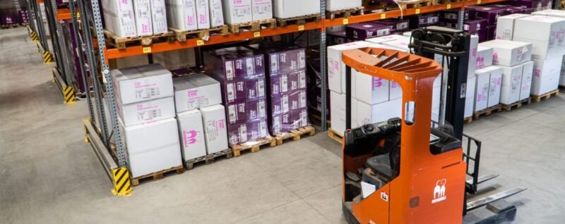 Ein orangefarbener Gabelstapler in einem Hochregallager mit gelagerten Kartons