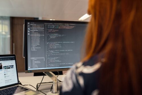 Eine Person bei der Arbeit am Computer vor einem Bildschirm mit Programmiercode