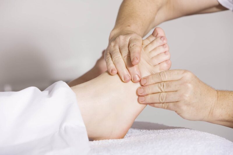 Hände eines Physiotherapeuten bei der Behandlung eines Fußes zur Veranschaulichung des Berufsfelds