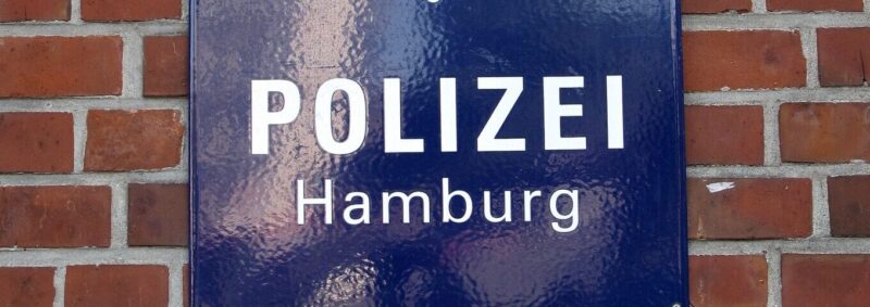 Blaues Schild mit der Aufschrift Polizei Hamburg an einer Backsteinwand