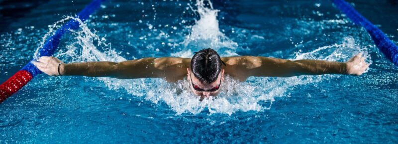 Schwimmer beim Schmetterlingsschwimmen in einer Schwimmbahn als Symbol für die Sporteignungsprüfung