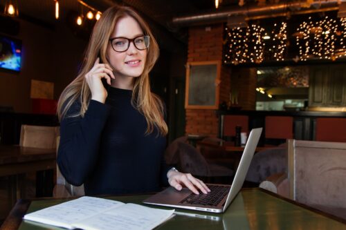 Junge Frau mit Brille telefoniert am Laptop beim Lernen für ein Studium