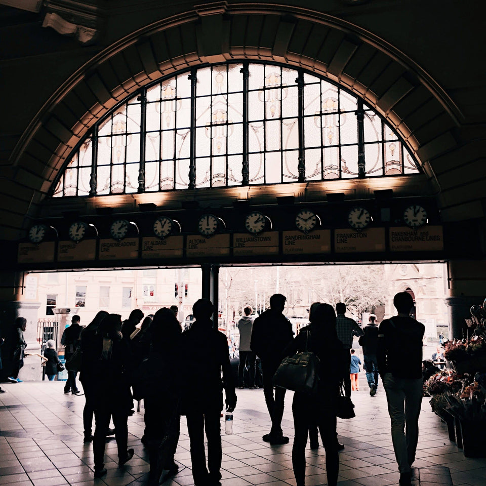 Menschen als Silhouetten in einer Bahnhofshalle unter Bahnhofsuhren zur Veranschaulichung des Arbeitsumfelds im Zugverkehr